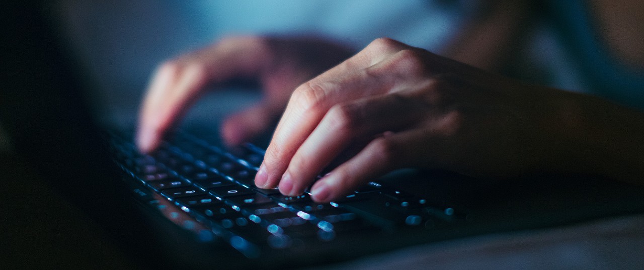 Close-up shot of female hands typing on computer keyboard, lying on bed, working late at home.